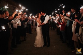 At their Budapest reception venue, the newlyweds share a romantic kiss beneath a glowing tunnel of sparklers, surrounded by cheering loved ones, as the sparkling lights illuminate the joyful night celebration.